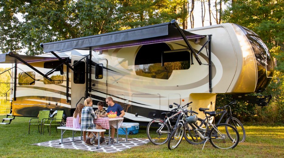 Family sits at picnic table underneath the awning on their fifth-wheel RV